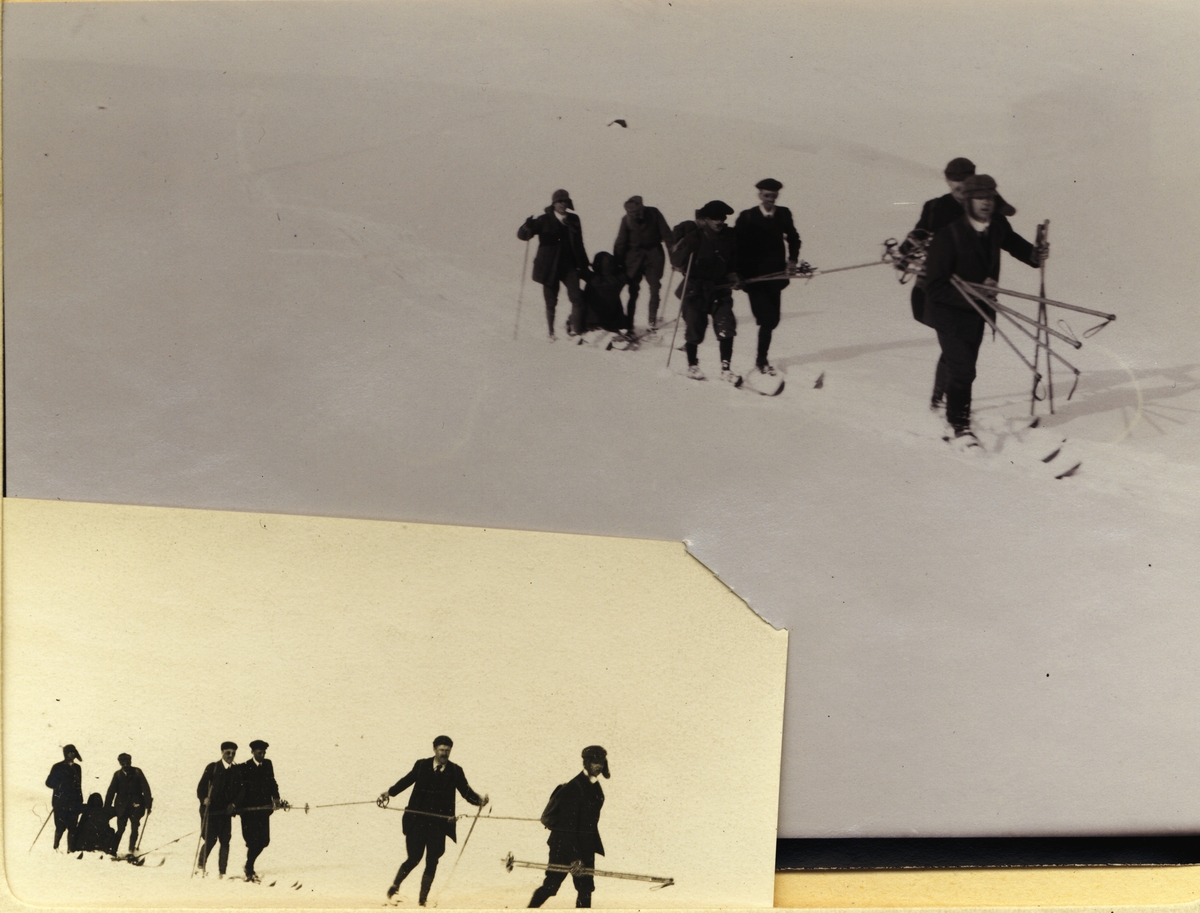 En skigåer, O. Bronn(?), med beinbrudd sitter på to sammenbundne ski og trekkes/skyves av seks andre skigåere. Fotografert i Jotunheimen i mars 1908.