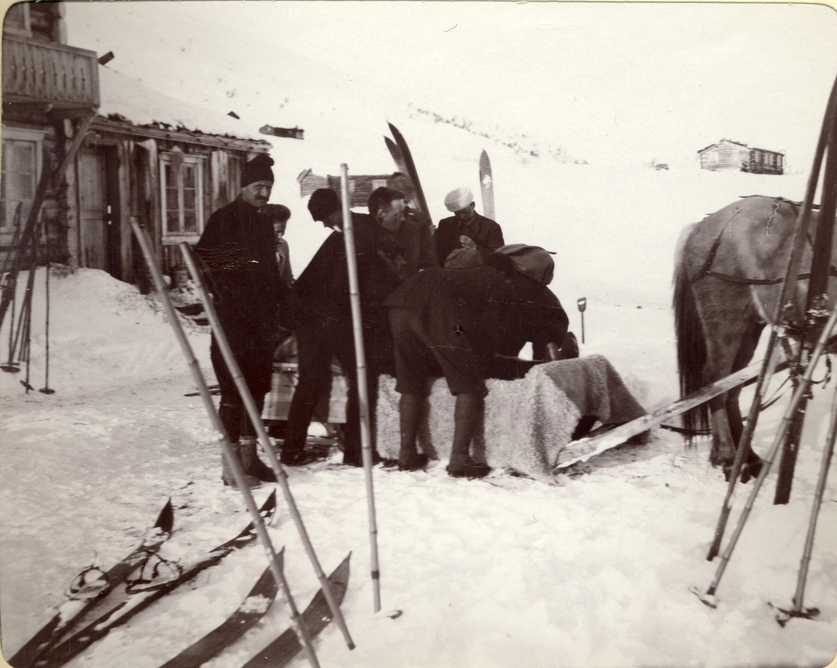 En skigåer med benbrudd, O. Bronn(?), blir anbragt på en hestetrukket slede utenfor turisthytten Bessheim i Jotunheimen. Fotografert mars 1908.