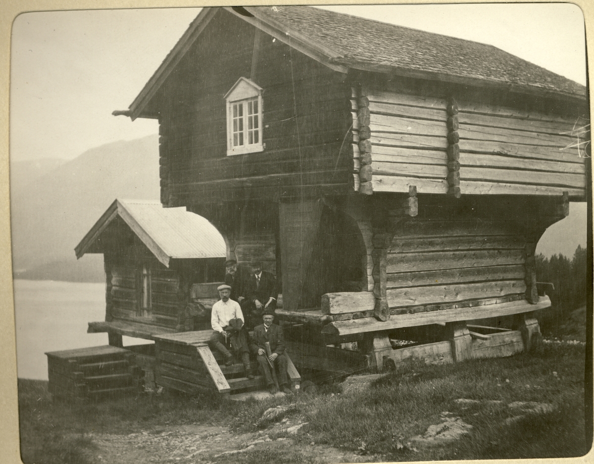 Fire menn sitter på trappen til stabbur på Vasstveit gård i Hovin, Telemark. Til venstre i lys skjorte antagelig Ferdinand Egeberg. I bakgrunnen skimtes Tinnsjøen. Fotografert 1908.