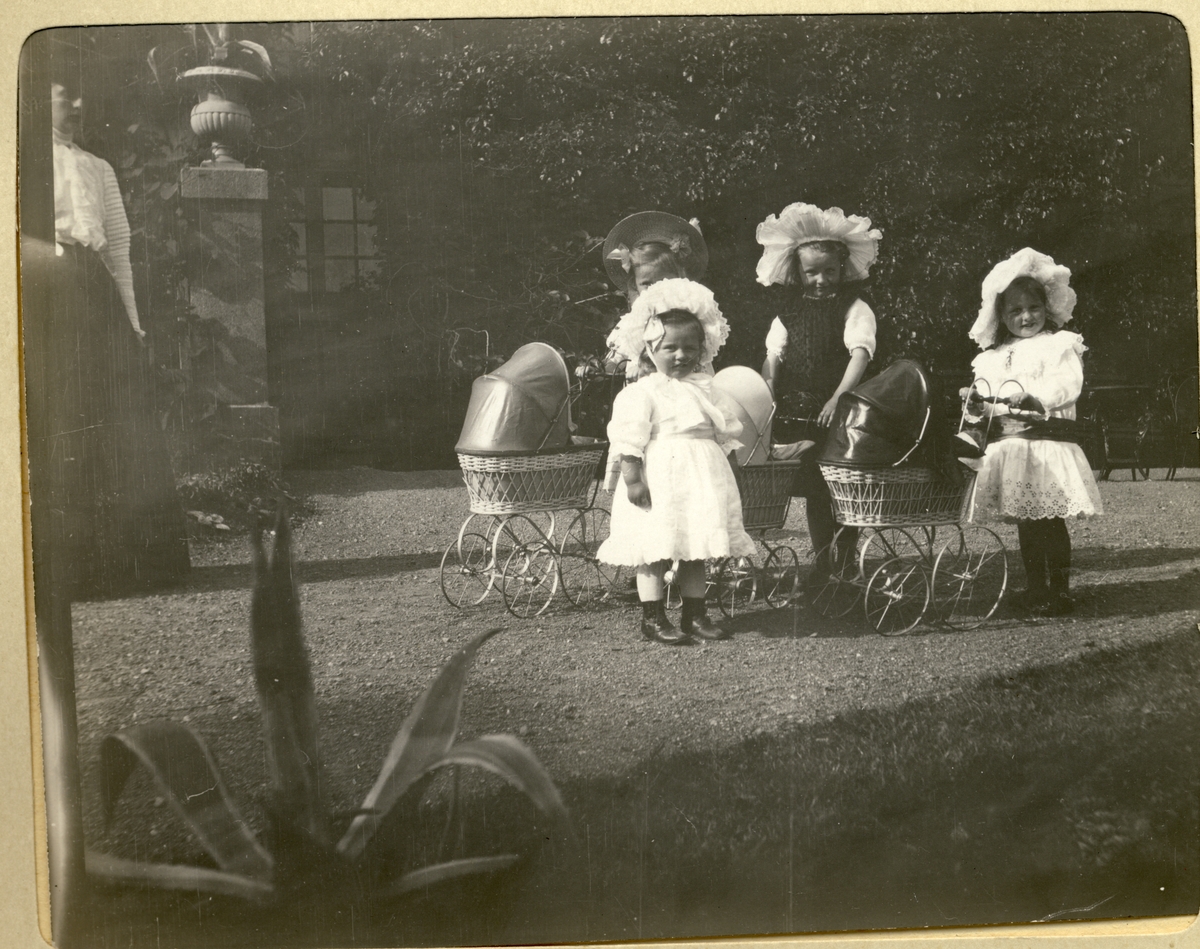 Mimi og Lucy Egeberg, i hvite kjoler, og to venninner triller dukkevogner i parken til Bogstad gård. Nini Egeberg skimtes til venstre i bildet. Fotografert juli 1909.