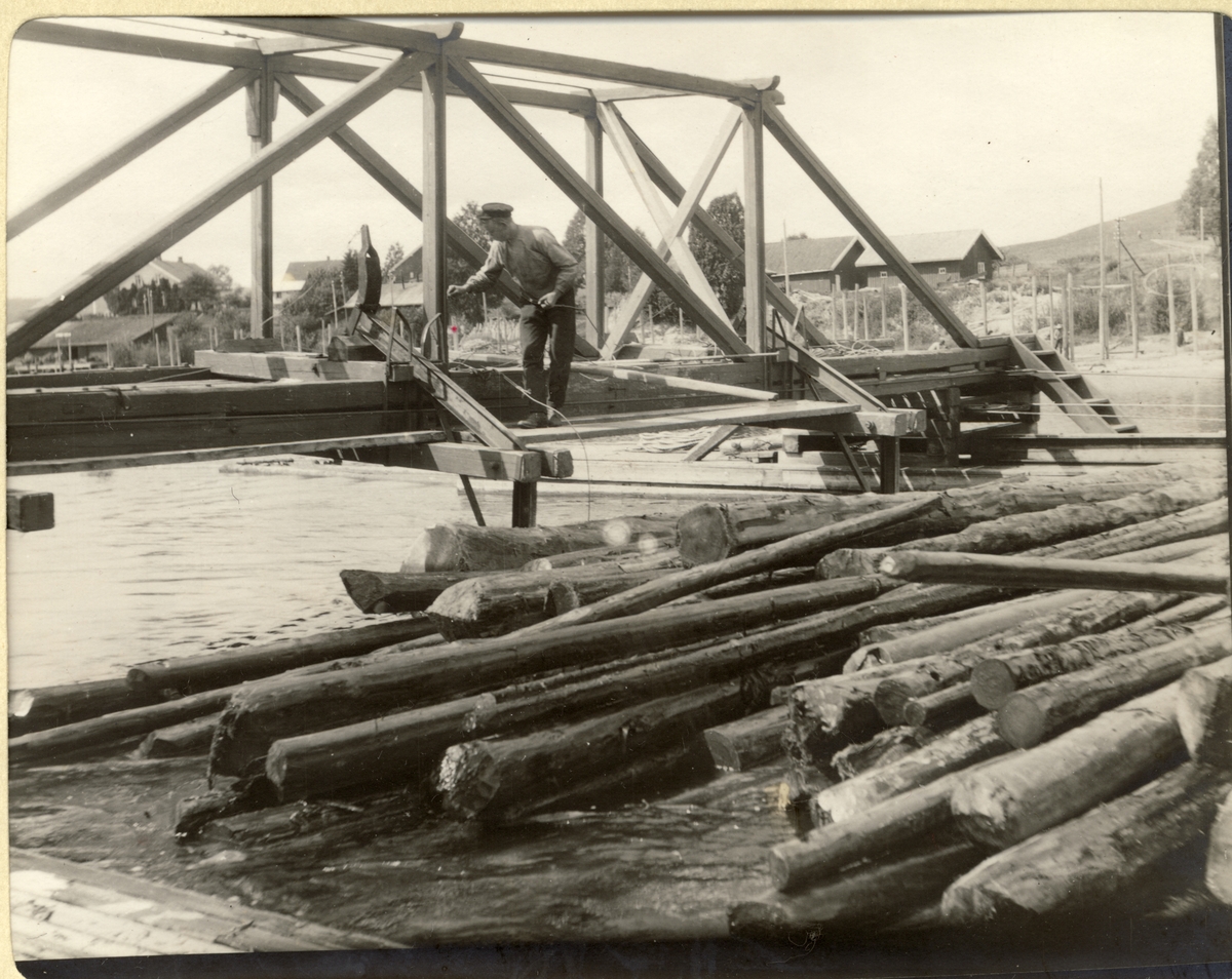 En mann opererer et soppeapparat, også kalt en mosemaskin, ved Fetsund lenser i Akershus. Maskinen komprimerer tømmeret før det bindes sammen ved hjelp av vaiere. Fotografert 1910.