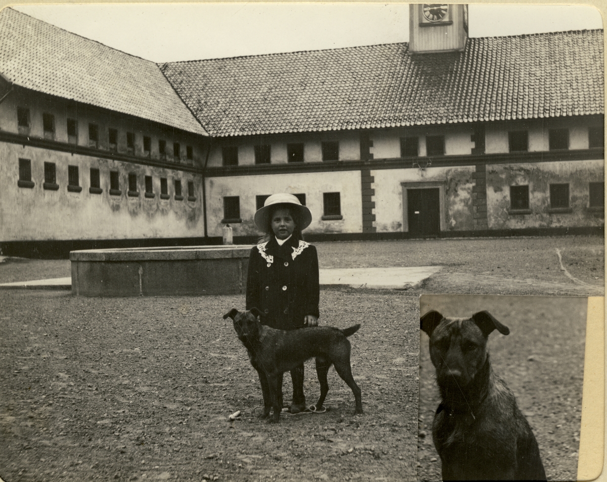 Mimi Egeberg med to hunder på gårdsplassen til Bogstad gård. Et fotografi av hunden er innfelt nederst i høyre hjørne. Antagelig fotografert 1911.