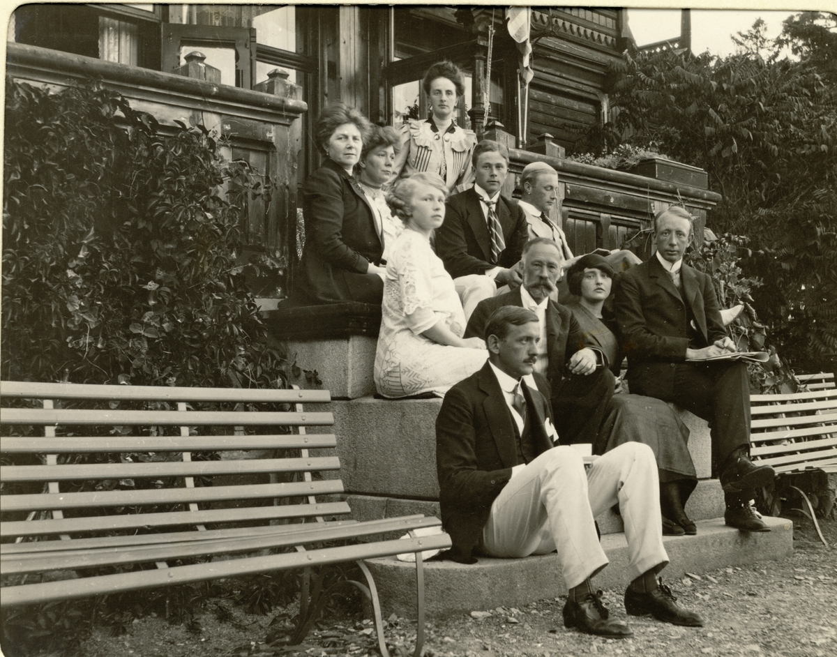 Familien Egeberg med flere samlet på verandatrappen til Lucy og Ferdinand Egebergs villa på Snarøya i Bærum. Fra venstre i øverste rekke og nedover: Lucy Parr Egeberg, Lilly Egeberg, Nini Egeberg, Ester Egeberg, Ferdinand P. Egeberg, Oscar Egeberg. Ferdinand P. Egeberg, Ingeborg Gude, Mohn(?), og Severin Finne. Fotografert 1911.