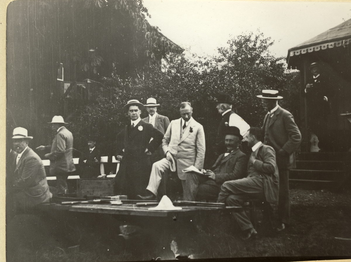 Medlemmer av Christiania Jægerklub har pause under skytetrening på Nakholmen i Oslofjorden. I bakgrunnen et bolighus og til høyre en slags tribune med baldakin. Fotografert 1912.