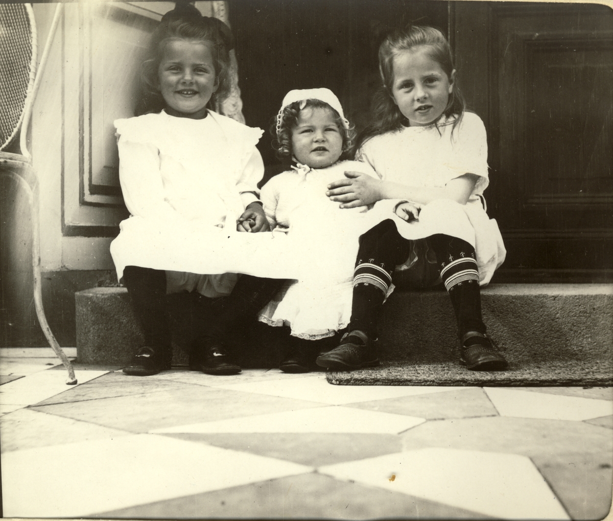 Søstrene Lucy, Karen og Mimi Egeberg sitter på et trappetrinn til veranda på Bogstad gård, Oslo. Fotografert 1912.