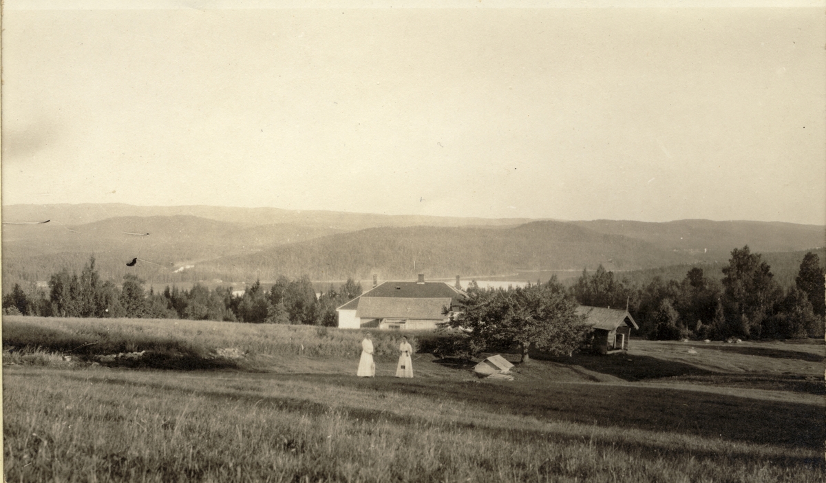 To kvinner, antagelig Nini Egeberg til høyre, står på jordene til Øiberget (Øyerberget?), Brandval Finnskog i Brandval kommune, Hedmark. Fotografert 1917.