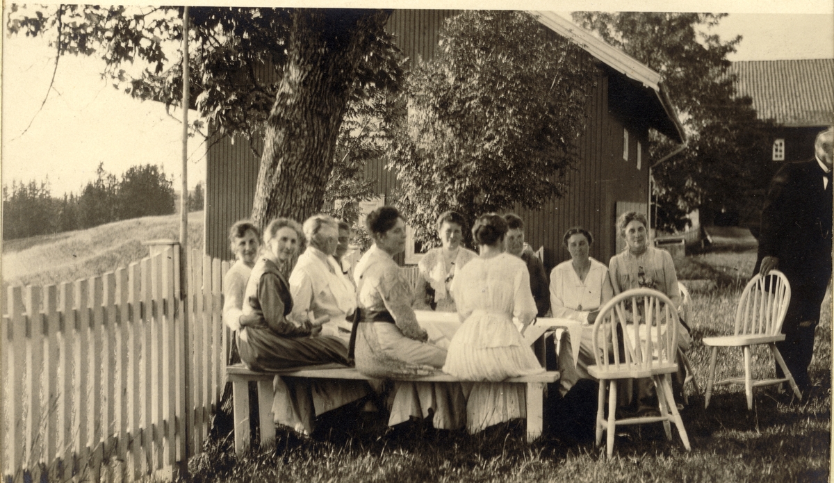 Gjester til feiringen av Lilla og Fredrik Giertsens sølvbryllup slapper av i hagen til et stort gårdstun, antagelig i Akershus. Fotografert 1918.