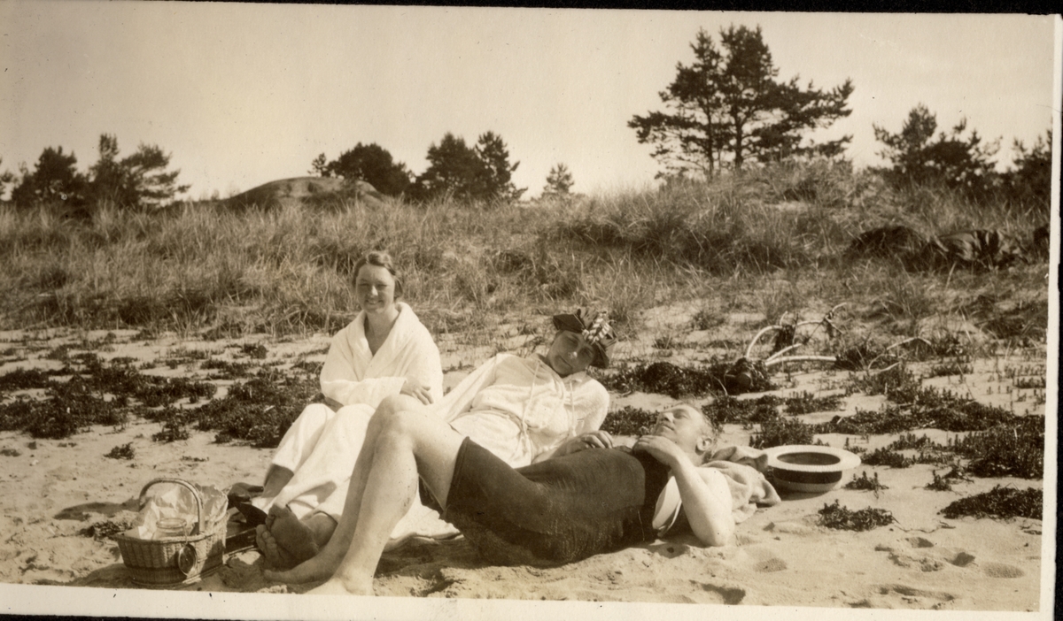 Tre personer nyter solen på sandstrand i Mandal. Fra venstre Dagny Plahte, Sossen (Sophie?) Lumholtz og Westye P. Egeberg. Fotografert juli 1922 i forbindelse med tur til Stavanger i seilbåten "Malva".