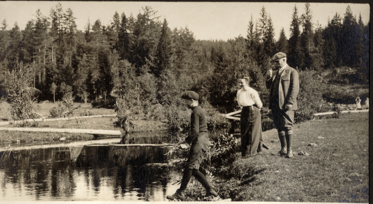 Herman S. Løvenskiold fisker kreps i Skinnarbølåa ved Kongsvinger. Faren Thorvald Løvenskiold og Nini Egeberg er tilskuere. Ukjent årstall.