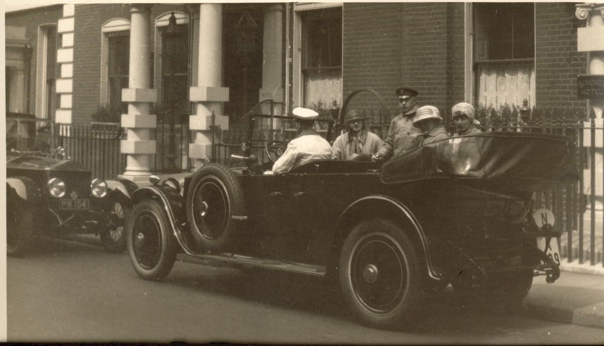 Thomas (Tom) Fearnleys bil med sjåfør uten for ukjent bygning, antagelig i London. Blant passasjerene er Westye P. Egeberg og Benedicte Fearnley samt Cecilie(?). Fotografert 1923.