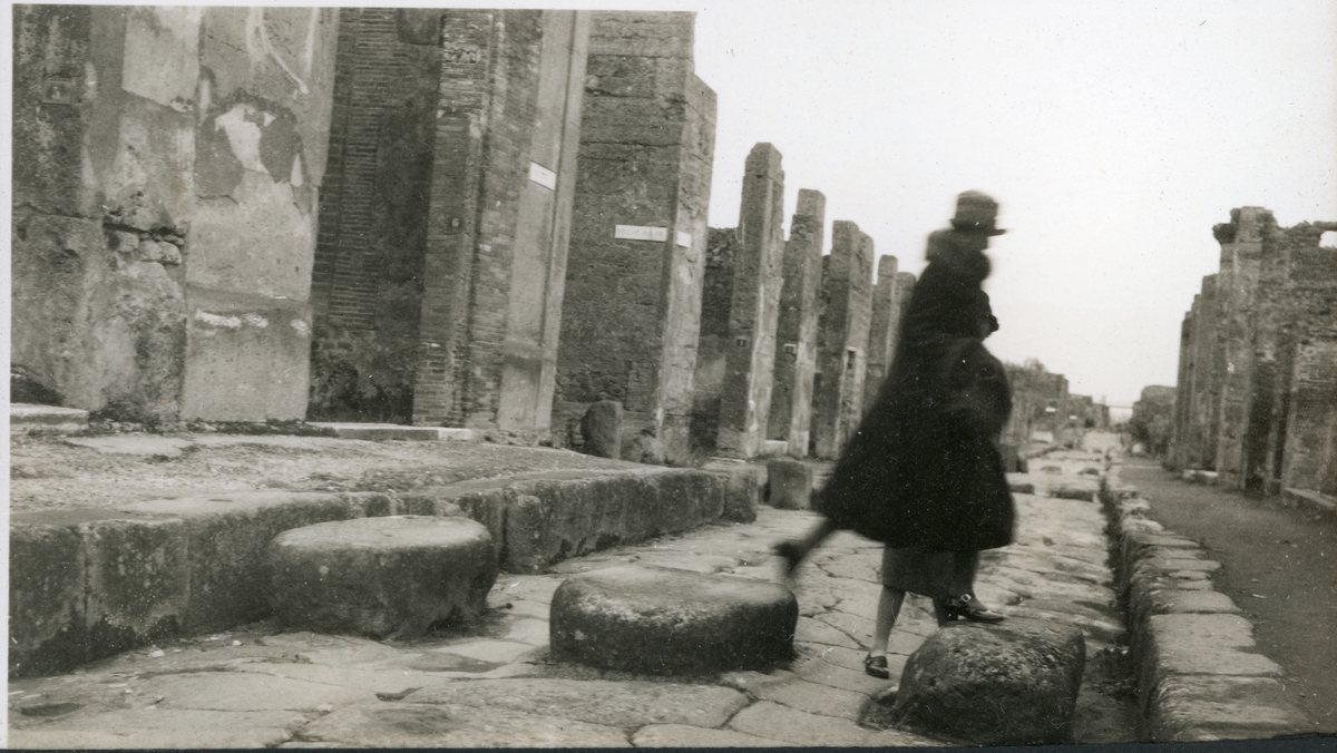 Nini Egeberg hopper fra stein til stein mellom ruinene i Pompei, under en rundreise i Italia i begynnelsen av februar 1927. Bak henne skimtes benet til en annen kvinne.