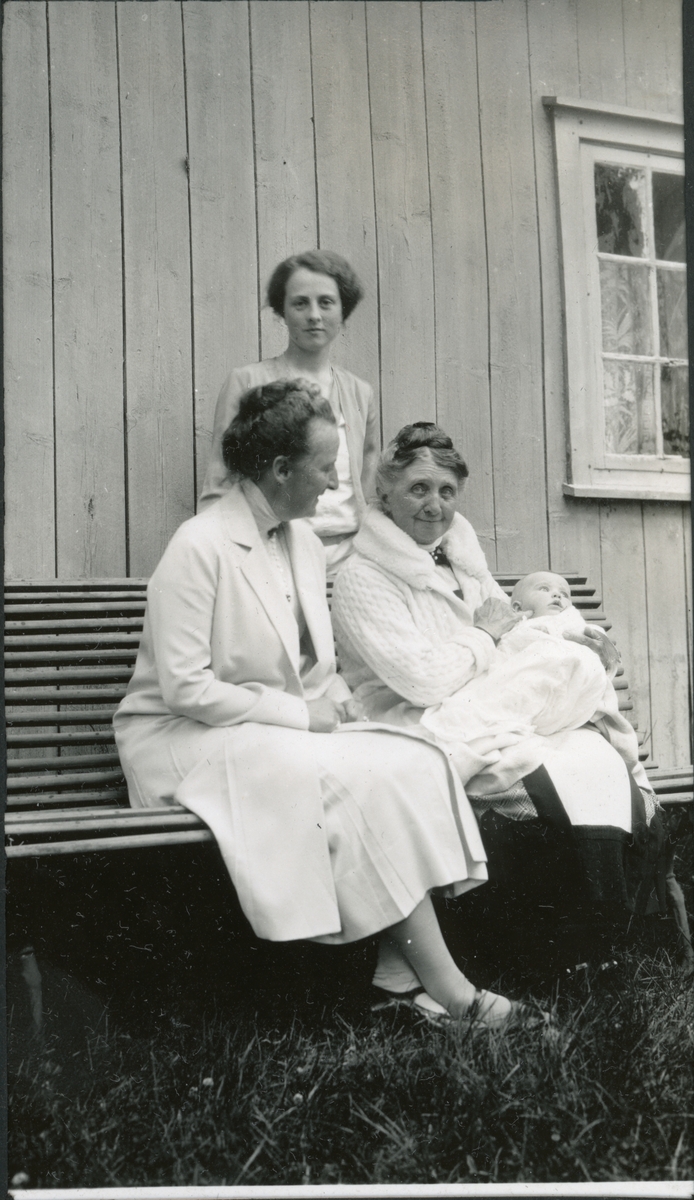 Fire generasjoner samlet i hagen på landstedet Fjugstad i Horten i forbindelse med Mimi Wedel Jarlsbergs fødselsdag. På benken sitter Nini Egeberg og hennes mor, Mimi Wedel Jarlsberg med oldebarnet Lucy Mathilde Hansson. Bak står barnets mor, Mimi Hansson. Fotografert 7. juli 1929.
