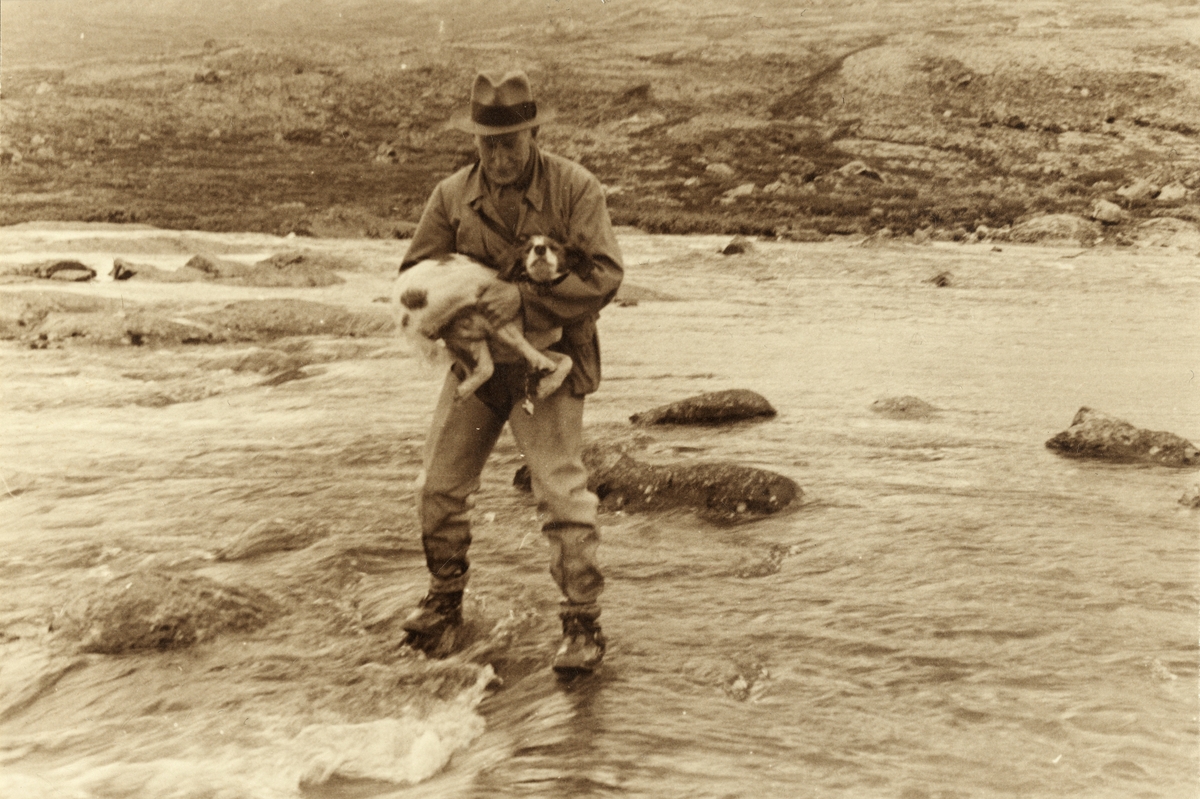 En turgåer, antagelig Carl Emil Rustad, redder sin hund i elven Russa i Vågå, Oppland.