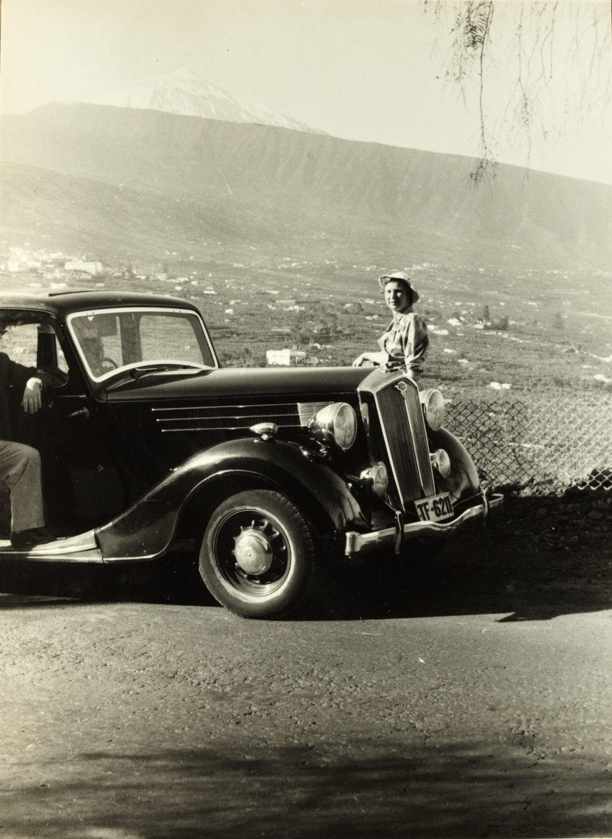 Evelyn Løvenskiold står ved bil på utsiktspunkt på Tenerife. Fotografert på cruise i 1953.