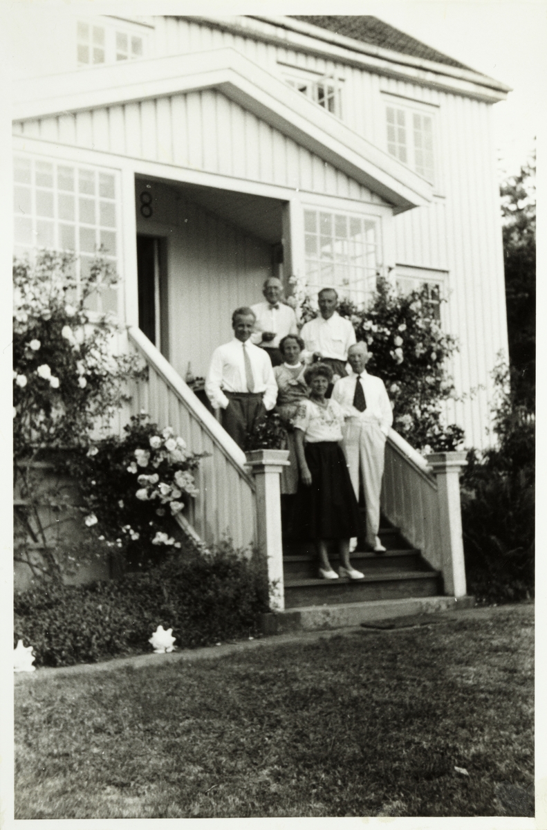Gruppebilde fra trappe på landstedet Dannevigen i Homborsund. Øverst står ambassadør Hans W.. Ahlson, dernest Rolf Grieg-Halvorsen Mimi og Sigurd Eek. Foran står Westye Parr Egeberg og fru Ahlson. Fotografert juli 1955.