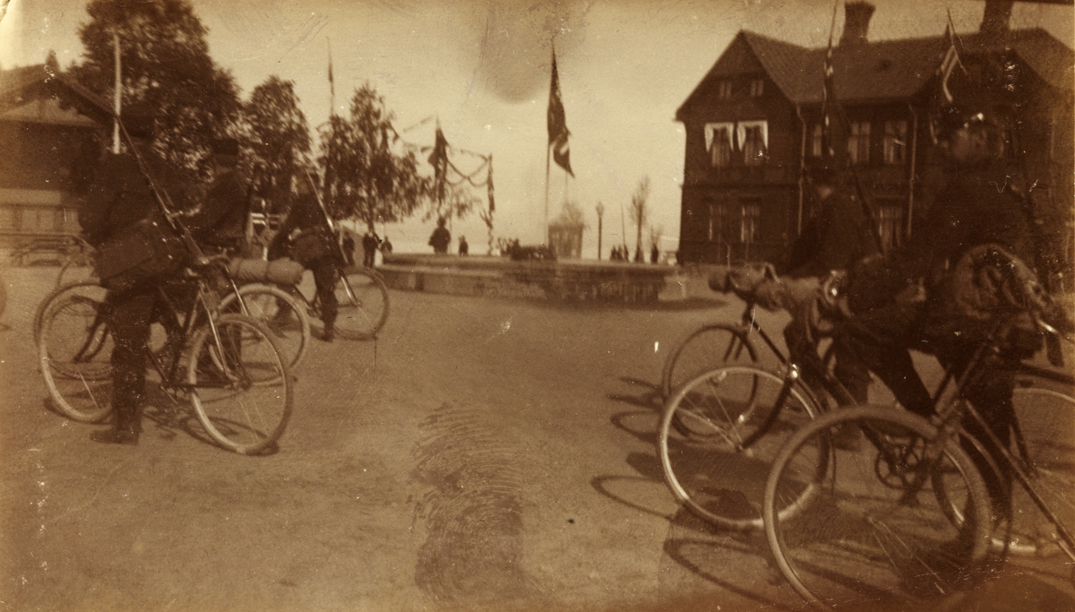 Soldater fra Søndenfjeldske Hjulrytterkompani sykler gjennom Levanger på vei fra Koppang til Værnes. Flagget er heist på torget. Fotografert 1901.