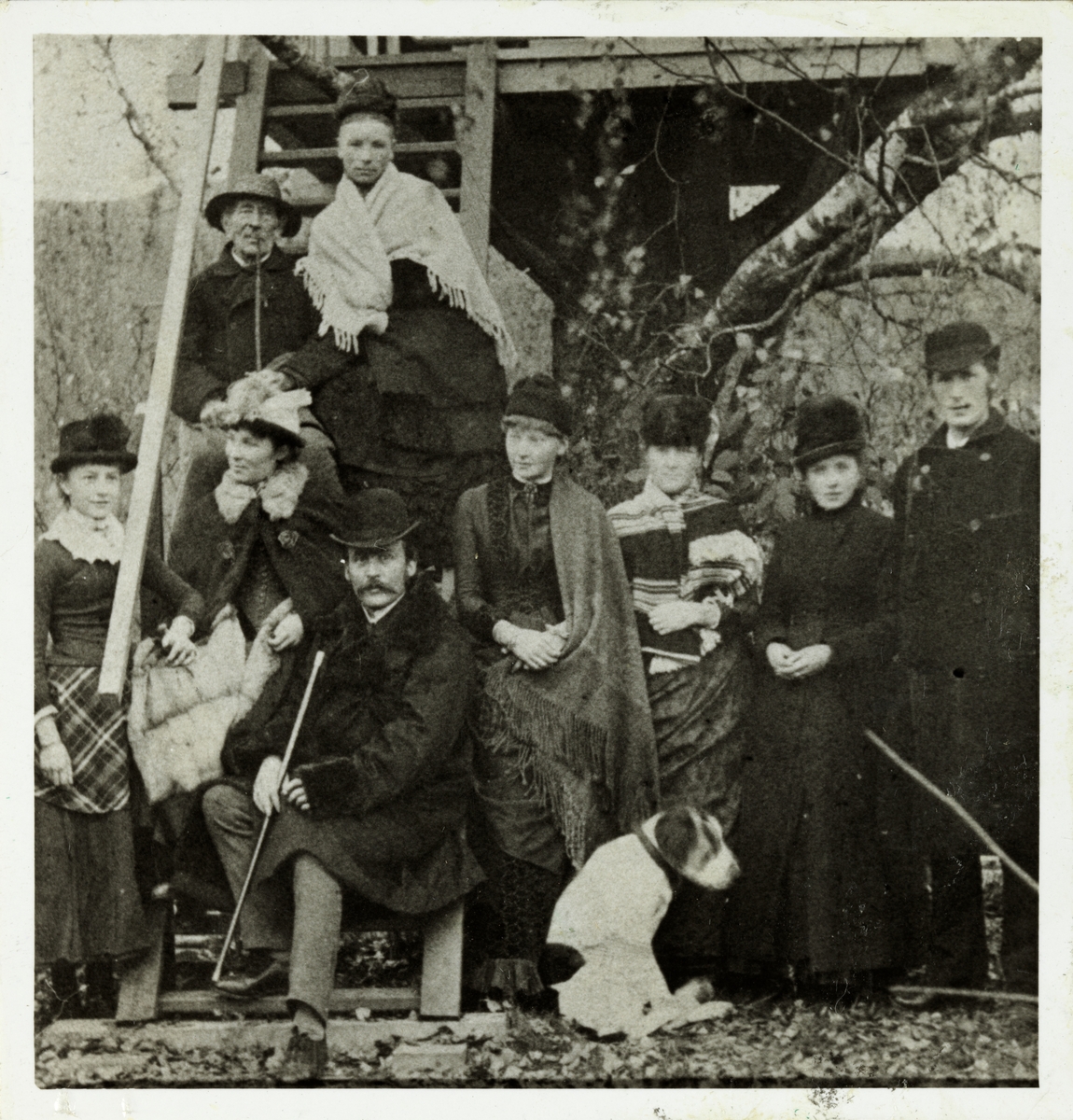 En gruppe kvinner og menn fotografert på Tannes i Nord-Odal, Hedmark. Øverst sitter konsul Westye Egeberg og husbestyrerinnen Josefine A. Bjurstedt. Nederst fra venstre Annette Gjertsen, Louise Ottesen, ukjent mann, Louise Gjertsen, Marie Ottesen samt Maren og Jørgen Müller. Ukjent årstall.