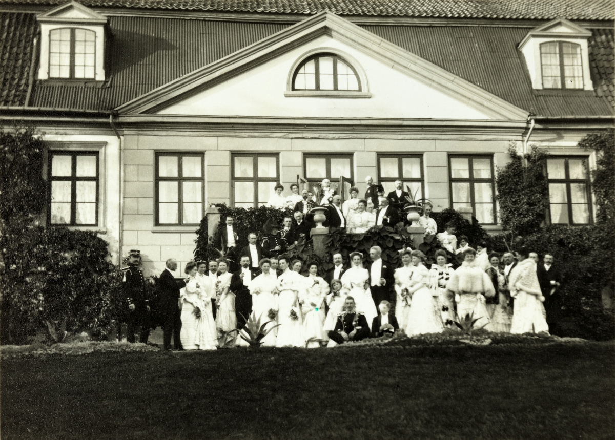 Brudeparet Nini, f. Wedel Jarlsberg, og Westye Parr Egeberg sammen med familie og andre bryllupsgjester (se foto med gjesteliste) foran hovedbygningen på Bogstad gård. Fotografert 17. september 1904. 