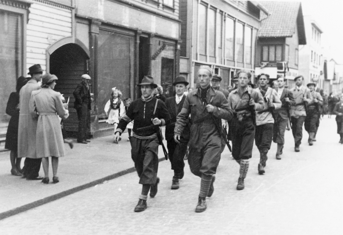 Feiring av freden 1945. Norske motstandsfolk med våpen marsjerer nordover Strandgt. Tilskuere på fortauet.