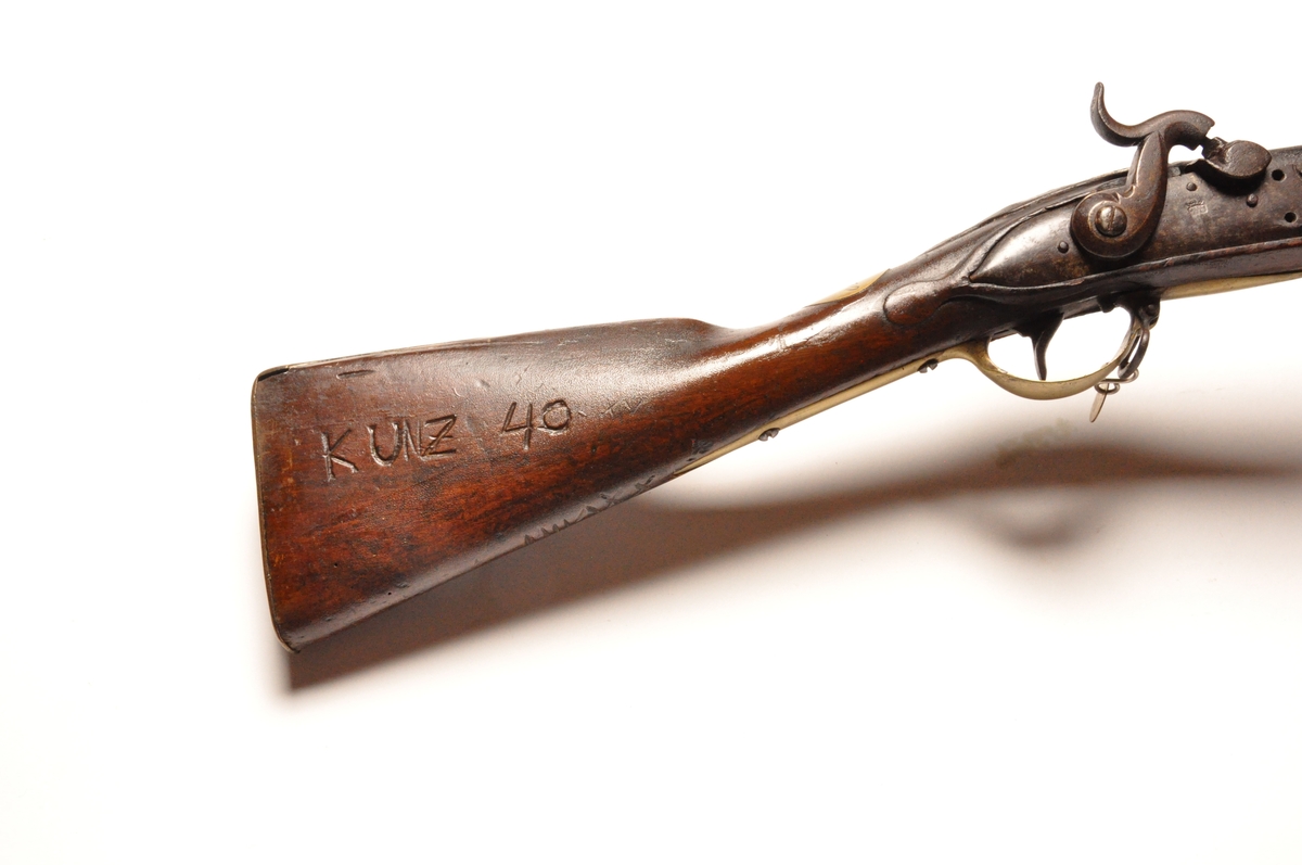 Glattløpet perkusjongevær av tre og metall med messingdetaljer. Flere innrissede merker og nummereringer. Opprinnelig militærvåpen.