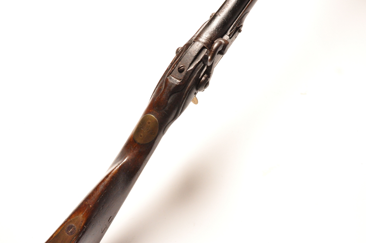 Glattløpet perkusjongevær av tre og metall med messingdetaljer. Flere innrissede merker og nummereringer. Opprinnelig militærvåpen.
