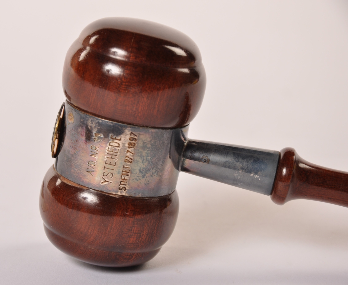 Styreklubbe i dreid, lakkert tre, beslått med metall og et emaljert merke. I pappeske (m/bomull) merket Gullsmed G. Langthon, Mysen.