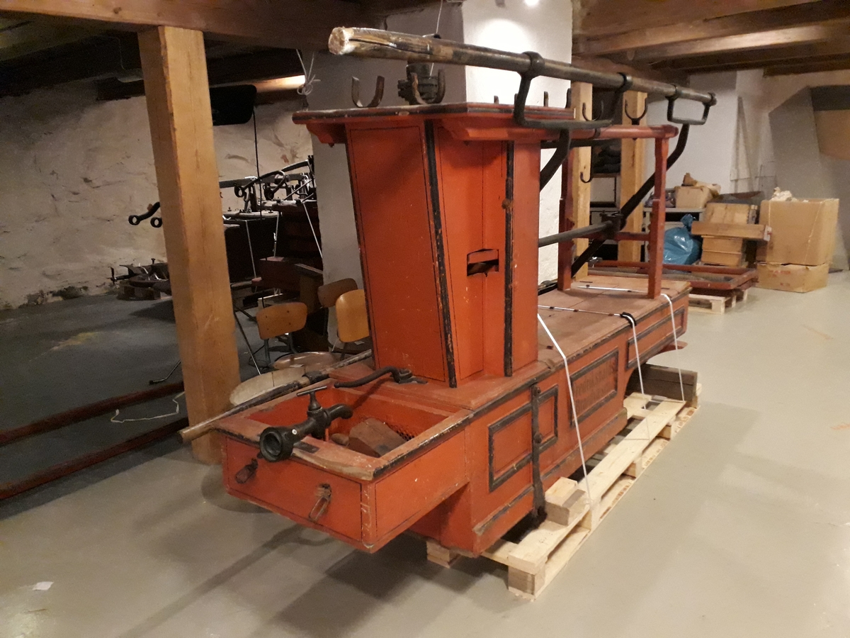 Pumpevogn av rødmalt tre med 4 jernbeslåtte hjul og drag til hest. Avlang kasse med lokk som inneholder pumpehus i metall. Rom foran, med lokk,  og bak, rommet bak har kran av messing som kan kobles til slange. Oppheng og bøyler med 2 slanger i tekstil, forsterka med metall. Langsgående pumpeanordning for håndpumping.