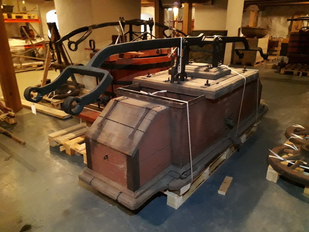 Pumpevogn av tre med 4 jernbeslåtte hjul, med ett drag. Rødmalt kasse i metall, med pumpeanordning i metall med pumpehus i tre. Kasse med lokk, av tre, foran og bak.