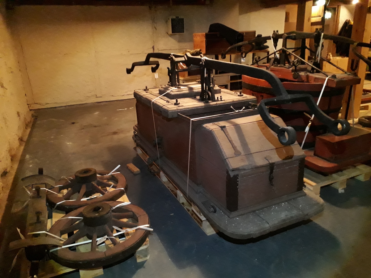Pumpevogn av tre med 4 jernbeslåtte hjul, med ett drag. Rødmalt kasse i metall, med pumpeanordning i metall med pumpehus i tre. Kasse med lokk, av tre, foran og bak.