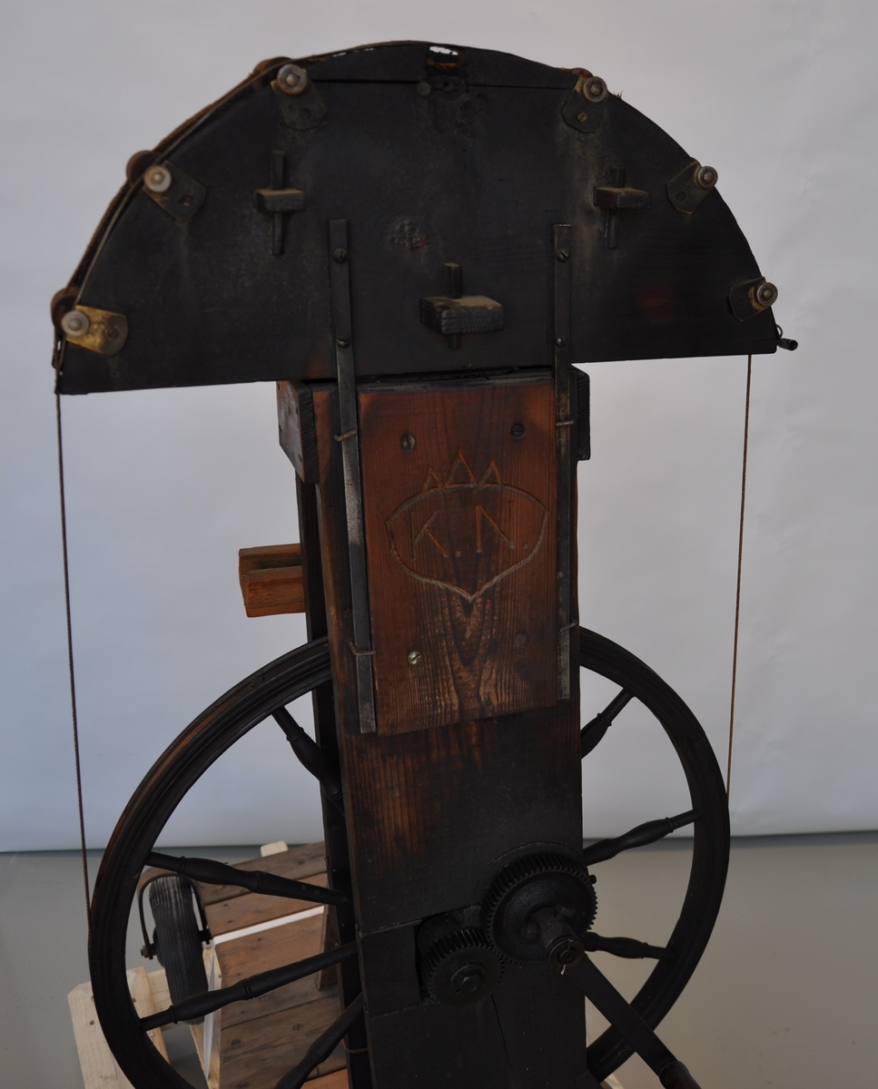 Vogn med repslagerhjul med krone, alt i tre. Trapesformet understell med 4 gummihjul. Metalldetaljer. Sveiv i tre og metall med tannhjulsoverføring til repslagerhjulet.
