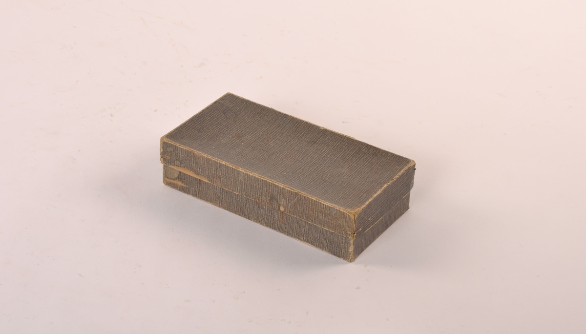 Eske av papp med lokk. Innehold: kapsler av porøst materiale.