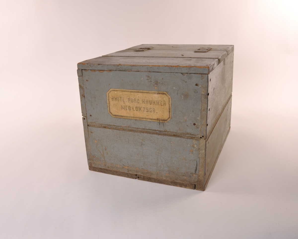 Rektangulær blågrå trekasse med flatt lokk med lær hengsler. Etikett, hvit med sort skrift.