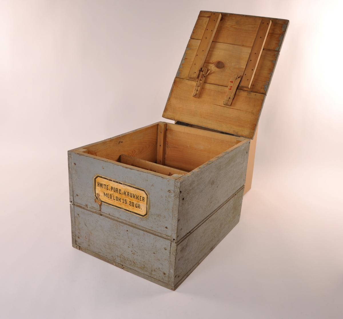 Rektangulær blågrå trekasse med flatt lokk med lær hengsler. Etikett, hvit med sort skrift. Ombygget lokk for større åpning.