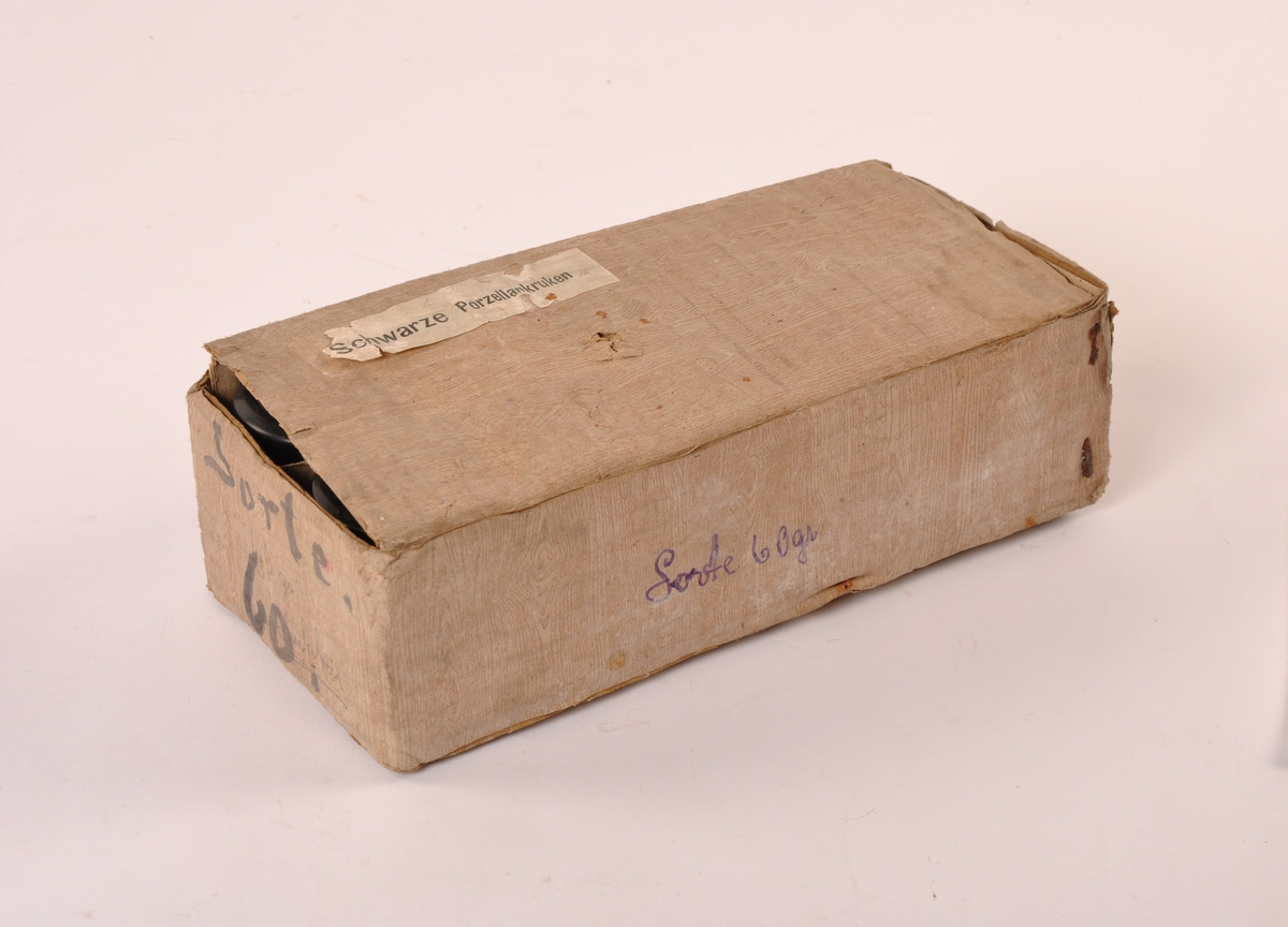 10 stk sylindriske krukker av sort porselen. Lokk av plast med apotekets logo i gull. I original embalasje av papp med årdring imitasjon