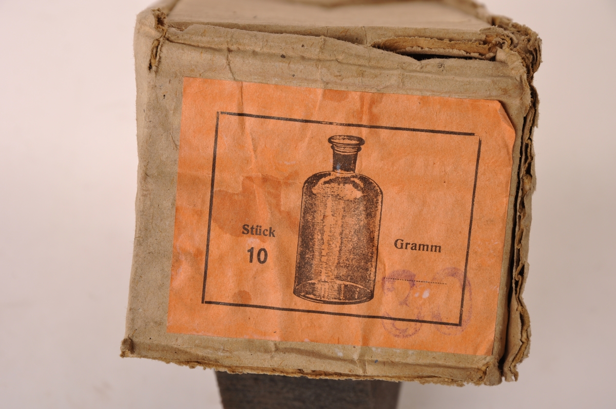 9 Stk sylindriske apotekerflasker av brunt glass med løs glasspropp. I original embalasje av papp, med etikett.