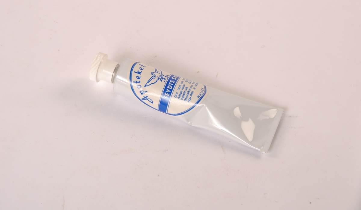 Tube i metall med plastkork. Tuben er tom.