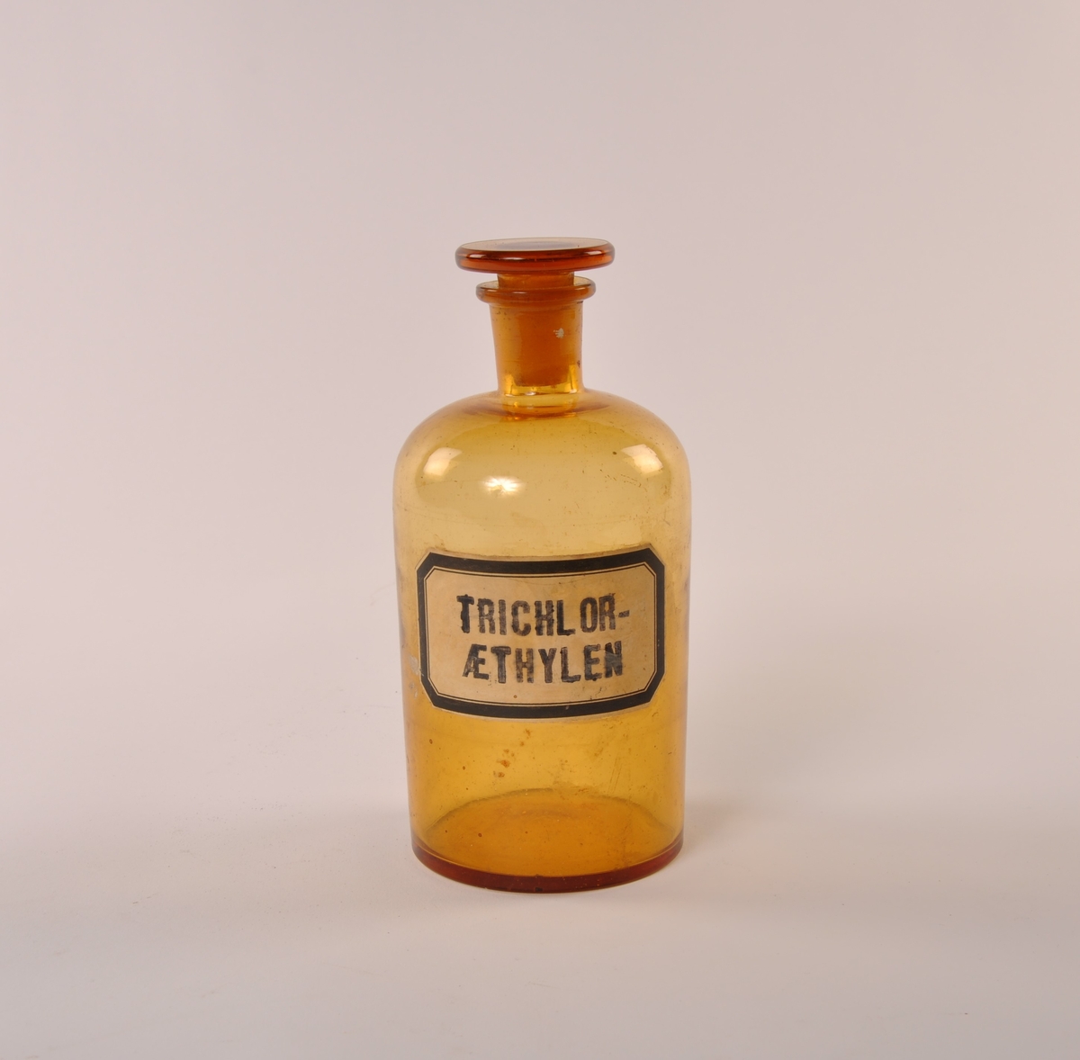 Flaske i brunt glass med rund hovedform, smalere tut og rund glasspropp.