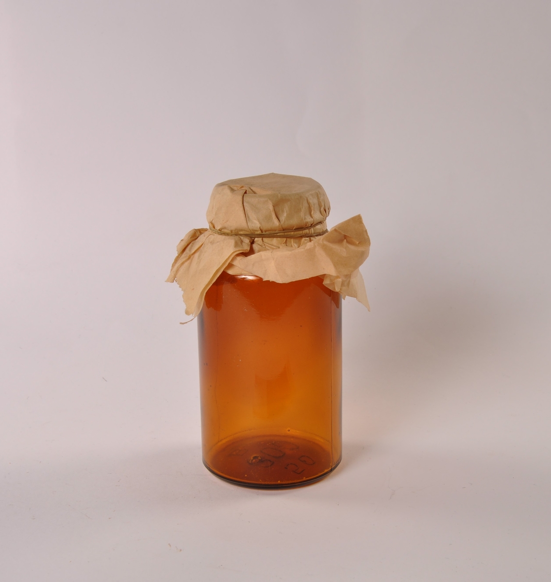 Krukke i klart glass med rund hovedform, smalere hals. Tildekket med papir festet med strikk.