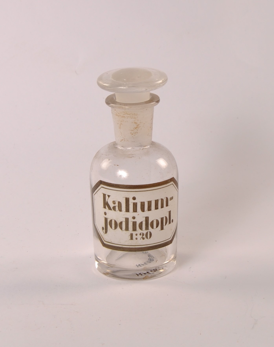 Flaske i klart glass. Rund form med smalere hals og munningsrand. Rund glasspropp.