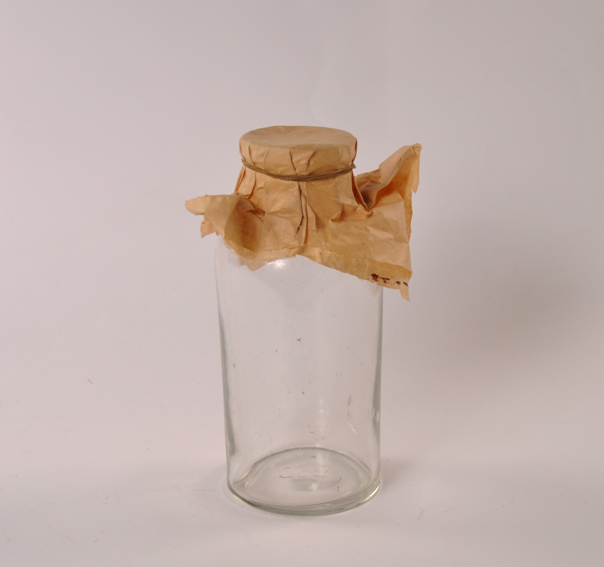 Krukke i klart glass med rund hovedform, smalere hals. Tildekket med papir festet med strikk.