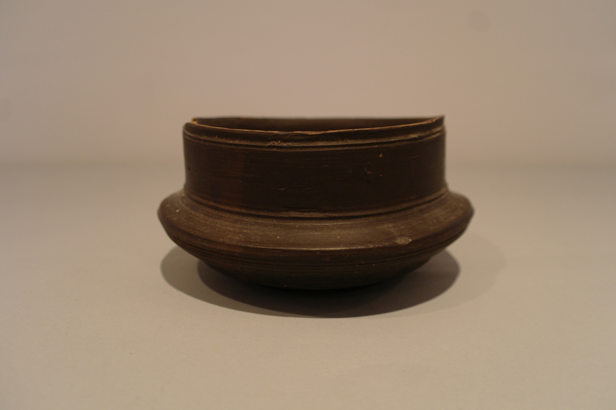 Brun dreiet bolle i tre. Sirkelforma munningsrand. Karet  svinger ut i ein vulst.  Eit lite hakk ved munningsranden.