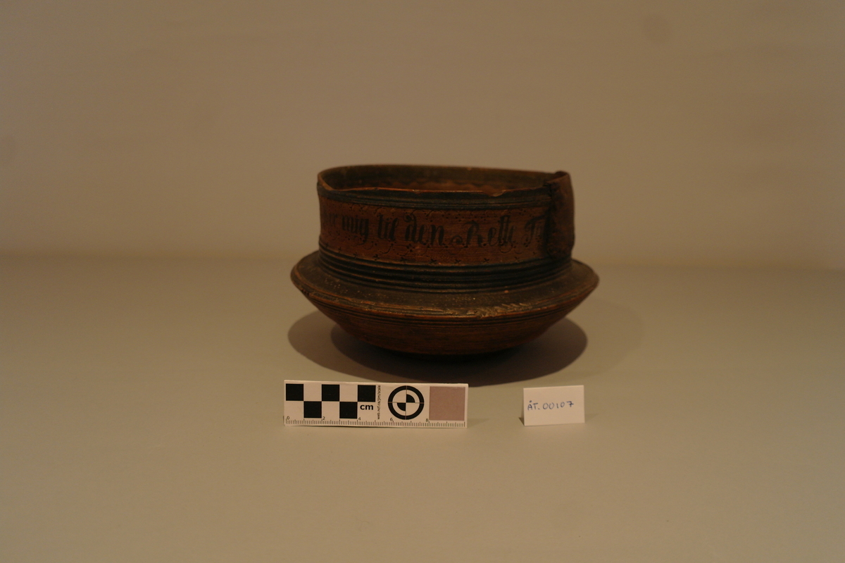 Dreiet bolle i tre. Sirkelforma munningsrand. Munningsranden er reparert med ein klinka plate av jarn. Bollen er måla med oker, svart, raud og blå. Den er dekorert med sviornamentikk og påmåla tekst.