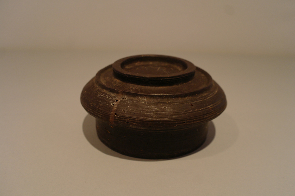 Brun dreiet bolle i tre. Sirkelforma munningsrand. Karet  svinger ut i ein vulst.  Eit lite hakk ved munningsranden.