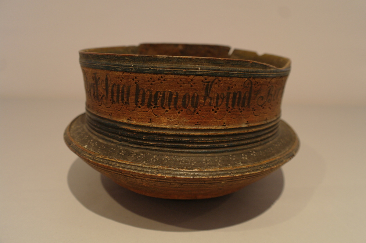 Dreiet bolle i tre. Sirkelforma munningsrand. Munningsranden er reparert med ein klinka plate av jarn. Bollen er måla med oker, svart, raud og blå. Den er dekorert med sviornamentikk og påmåla tekst.