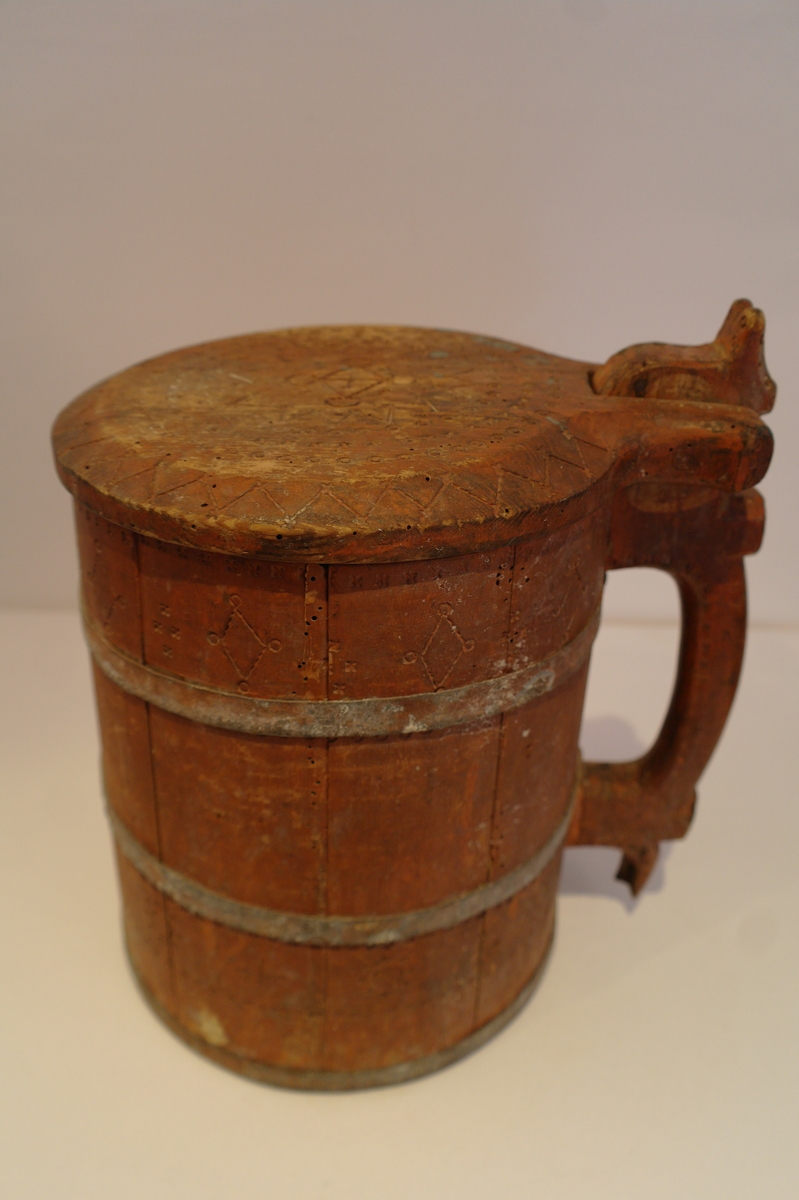 Lagga kar holdt saman av tre sinkband. Hanken er skrudd fast. Loket er hengsla til hanken med ein tretapp. Stavane, hanken og loket er dekorert med innrissa border,sirkler, spekulasjer og små blomer. Hanken er skåre ut i ein dekorativ fasong. Kanna er målt i ein raudbrun farge. I god stand. Nokre få hol etter mit.