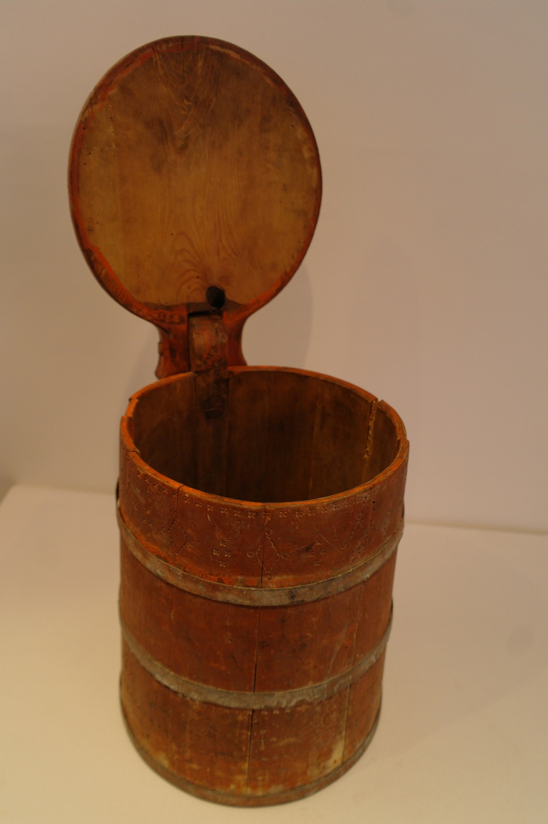 Lagga kar holdt saman av tre sinkband. Hanken er skrudd fast. Loket er hengsla til hanken med ein tretapp. Stavane, hanken og loket er dekorert med innrissa border,sirkler, spekulasjer og små blomer. Hanken er skåre ut i ein dekorativ fasong. Kanna er målt i ein raudbrun farge. I god stand. Nokre få hol etter mit.