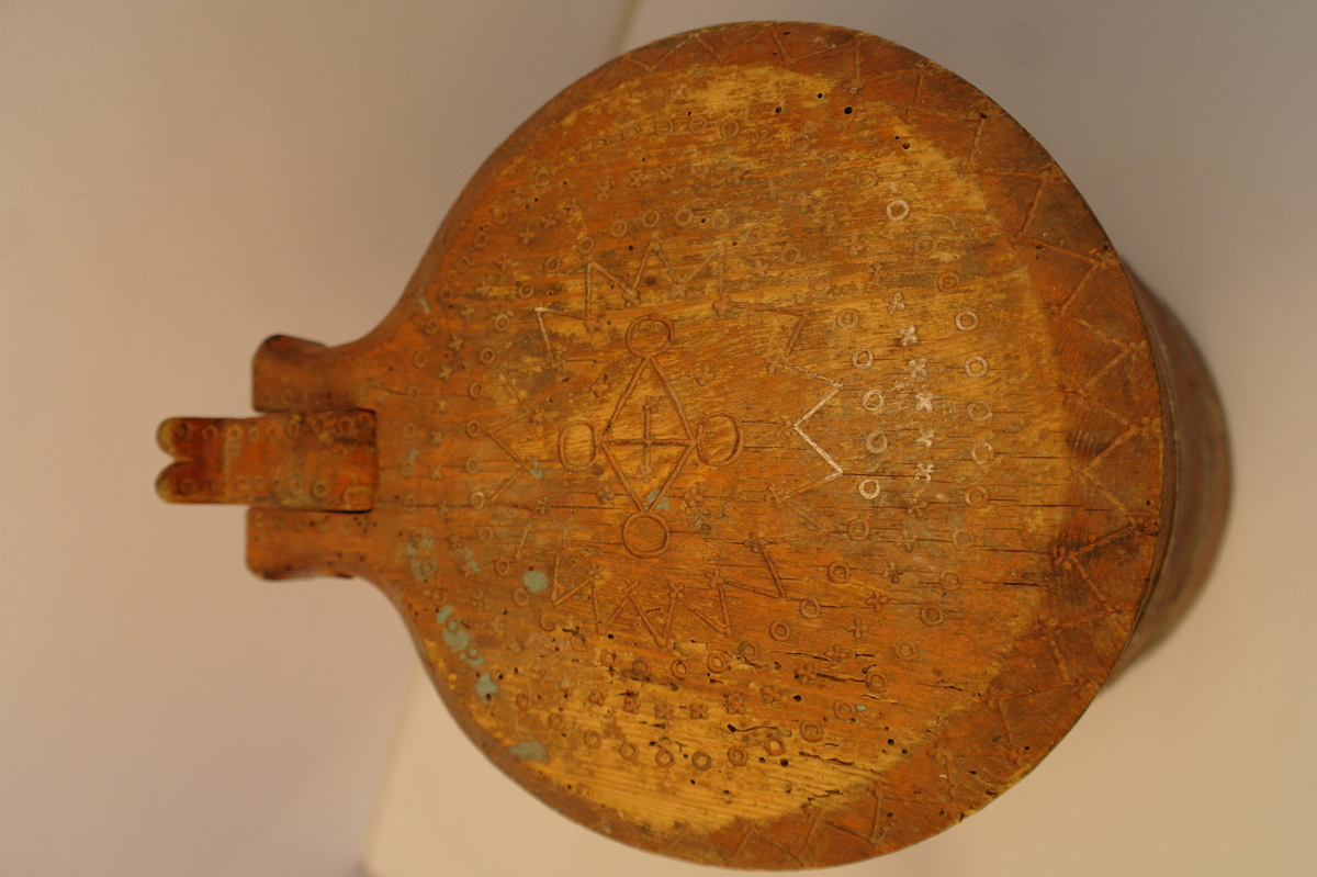 Lagga kar holdt saman av tre sinkband. Hanken er skrudd fast. Loket er hengsla til hanken med ein tretapp. Stavane, hanken og loket er dekorert med innrissa border,sirkler, spekulasjer og små blomer. Hanken er skåre ut i ein dekorativ fasong. Kanna er målt i ein raudbrun farge. I god stand. Nokre få hol etter mit.