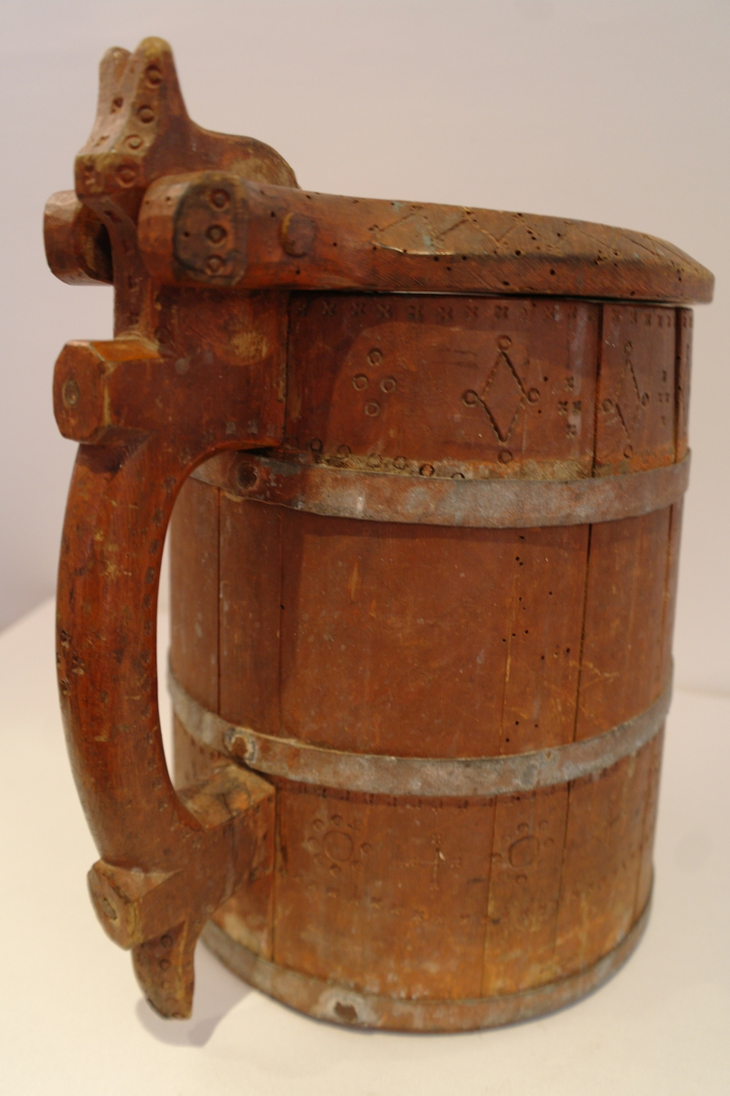 Lagga kar holdt saman av tre sinkband. Hanken er skrudd fast. Loket er hengsla til hanken med ein tretapp. Stavane, hanken og loket er dekorert med innrissa border,sirkler, spekulasjer og små blomer. Hanken er skåre ut i ein dekorativ fasong. Kanna er målt i ein raudbrun farge. I god stand. Nokre få hol etter mit.