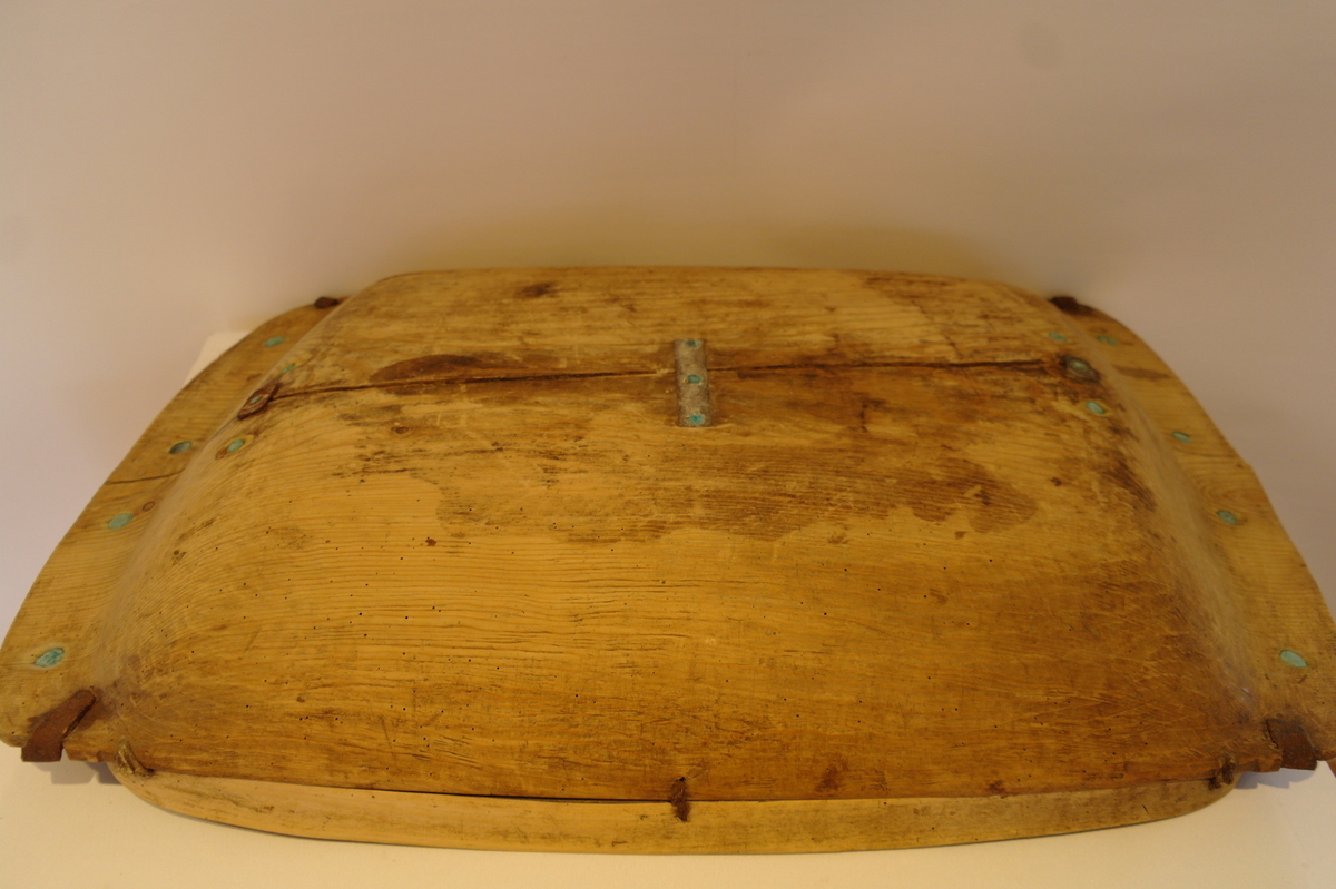 Trau i tre. Hola ut av eit stykke. Rektangulær og med runda buk. Handtaka på kortsidene er beslått med jarn. Ein stor sprekk går på langs frå handtak til handtak. Den er reparert med tre jarnbeslag. På den ene langsida er det satt på eit "skvettbord" festa med tau og spikrar.