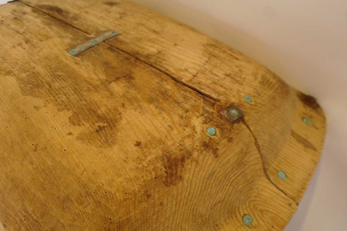 Trau i tre. Hola ut av eit stykke. Rektangulær og med runda buk. Handtaka på kortsidene er beslått med jarn. Ein stor sprekk går på langs frå handtak til handtak. Den er reparert med tre jarnbeslag. På den ene langsida er det satt på eit "skvettbord" festa med tau og spikrar.